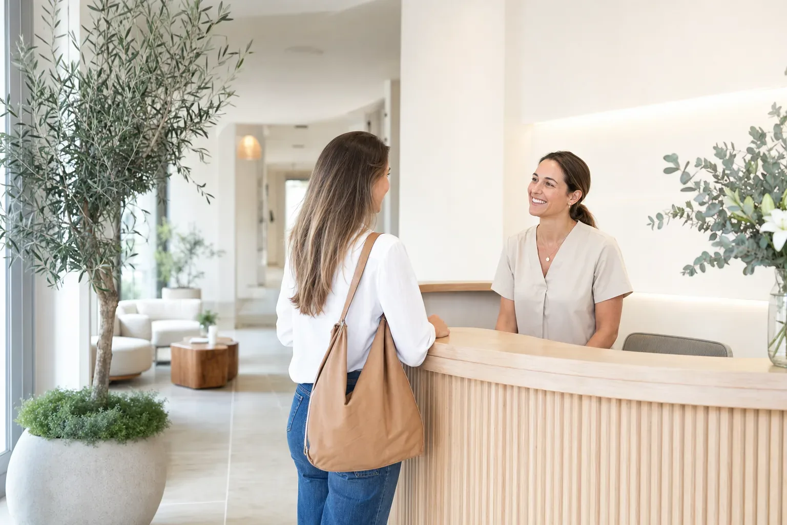 Recepción luminosa de una clínica de medicina estética donde la recepcionista recibe a una paciente.