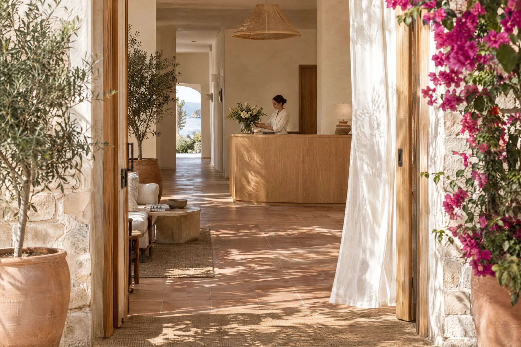 Entrada luminosa de un hotel boutique con buganvilla y recepción al fondo.