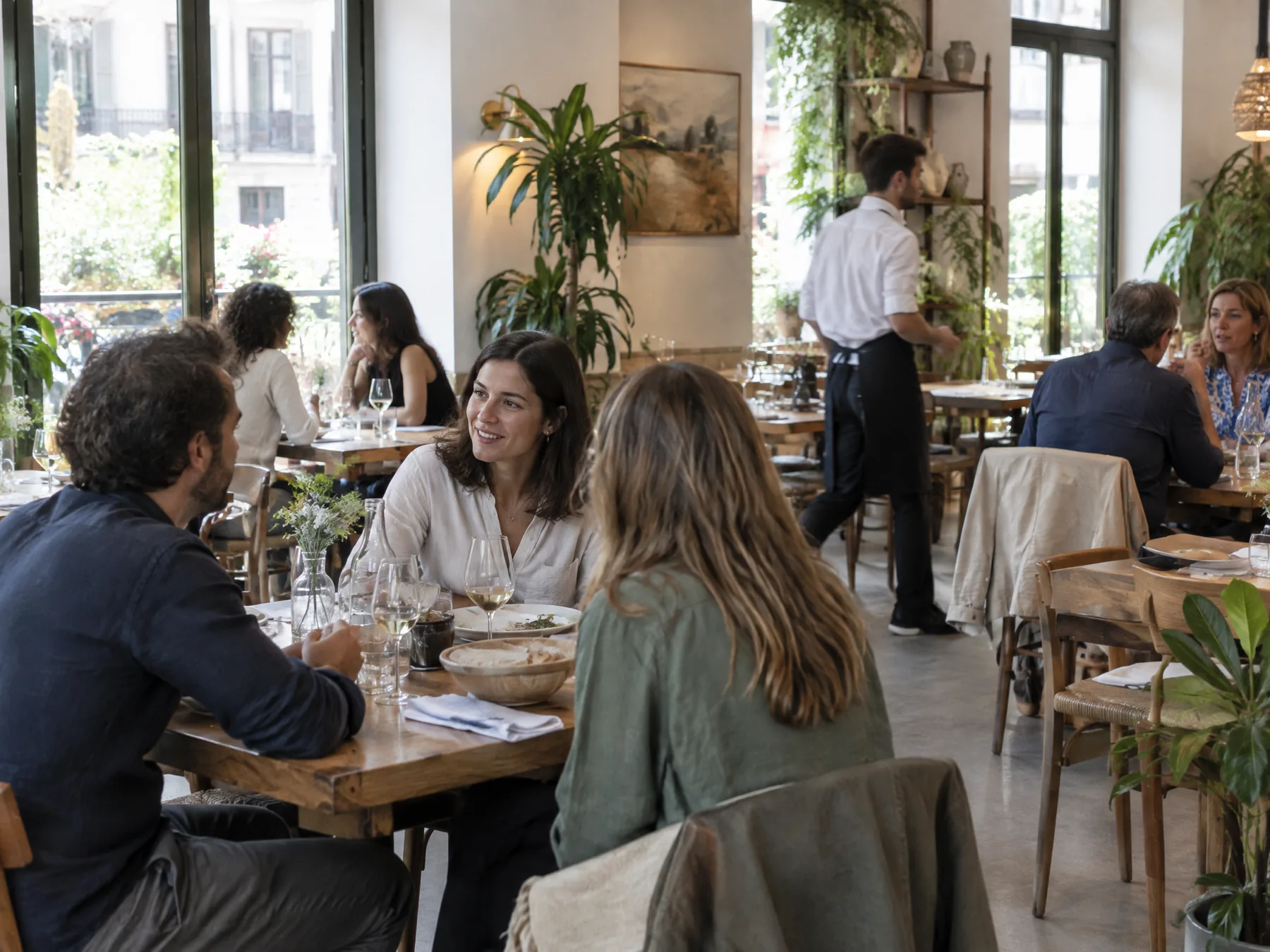 Comedor luminoso de un restaurante de barrio a mediodía, con clientes conversando y un camarero al fondo.